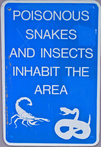 Road sign in blue, stating "Snakes and insects inhabit the area" with a diagram of a scorpion and a snake underneath.