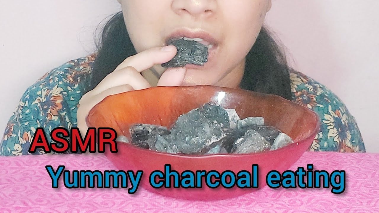 lower half of woman's face eating a lump of charcoal from a bowl of charcoal lumps. Text: ASMR - Yummy Charcoal Eating