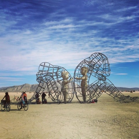 A Burning Man Sculpture - two wirework people facing away from each other, sad. Inside them, two scupltures of little children, reaching for each other.