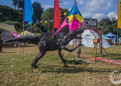 A dinosaur art work sits in front of a vibrantly coloured theme camp on the Paddock
