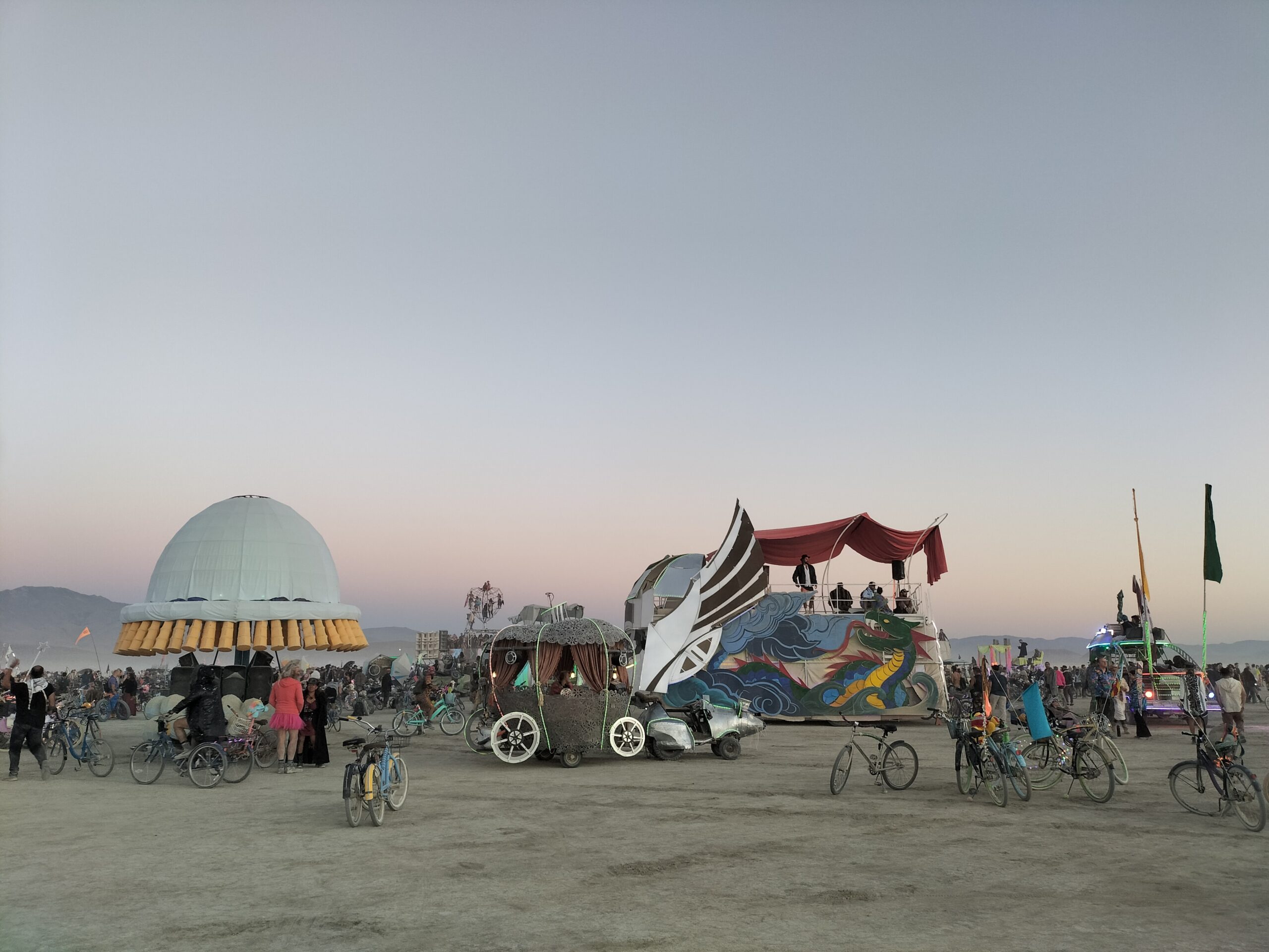 Art Cars and bikes scatter the desert with a fading clear blue sky in the background