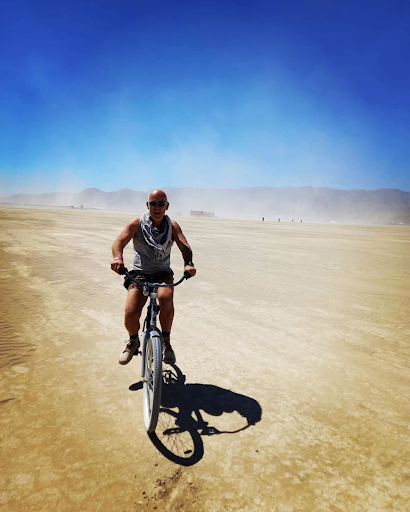 Paul sits atop his bicycle on the Playa with a hazy dust around him and clear blue skies in the background