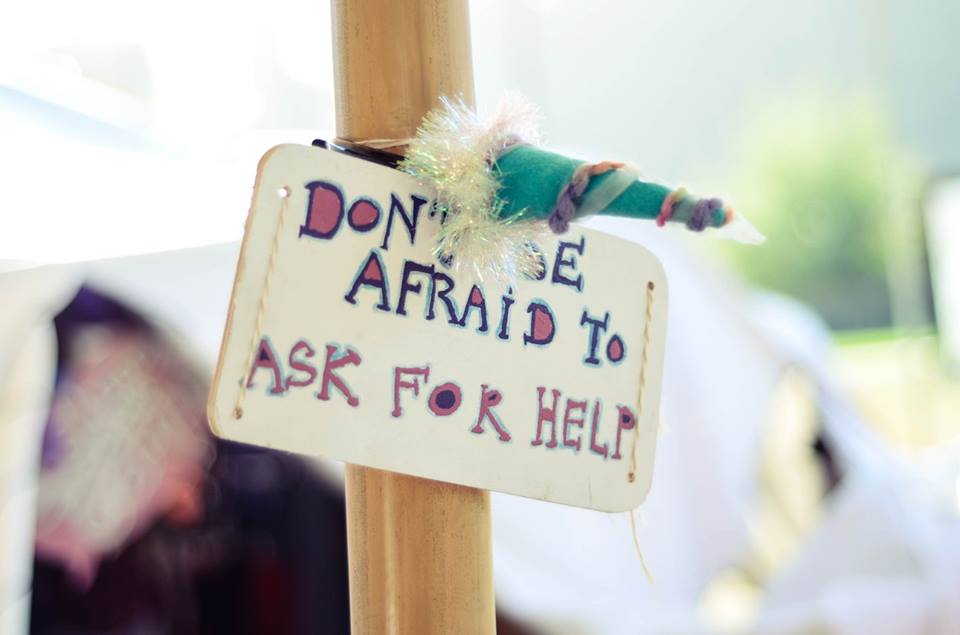 A white sign with colourful letters saying "don't be afraid to ask for help" with a blue unicorn horn above it