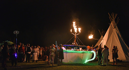 A huge tea cup with an LED light up rim, surrounded by people, sporting a trio of candle-like flames from its centre