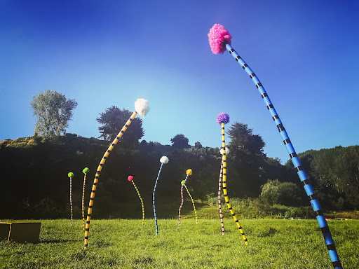 Brightly coloured, large fuzzy balls stand tall on colourful striped sticks with clear blue sky in the background