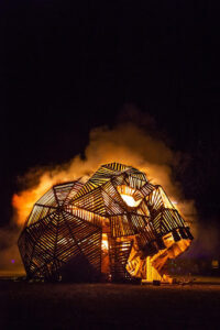 The 2023 Effigy, a wooden skull, has just been lit and sits engulfed in flames against a black sky