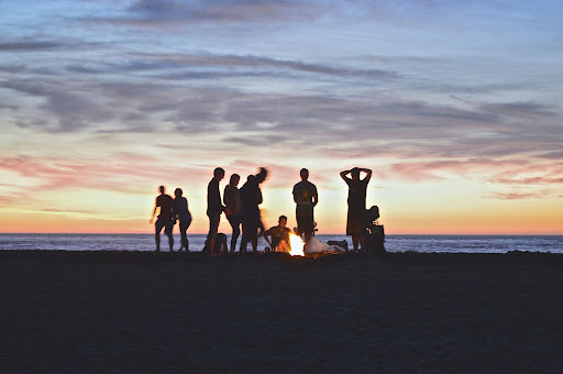 A silhouette of a group of people sitting around a fire on a beach at sunset