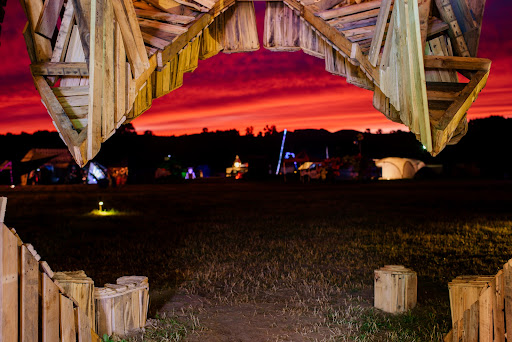 From inside the Skull Effigy we see wooden teeth and the lit up Paddock at sunset beyond