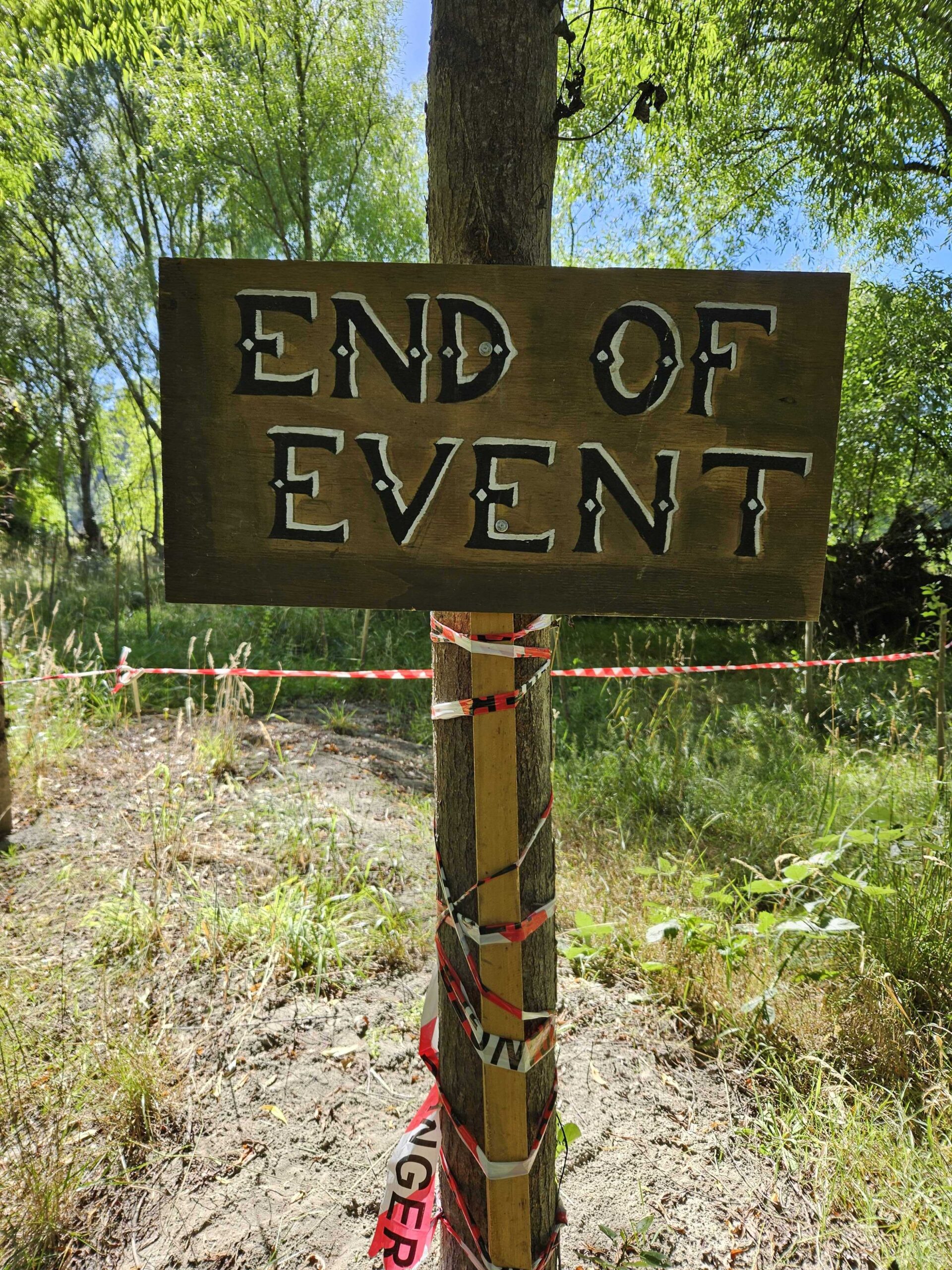 a wooden sign in a forest with caution tape around the post of it reads 'end of event'