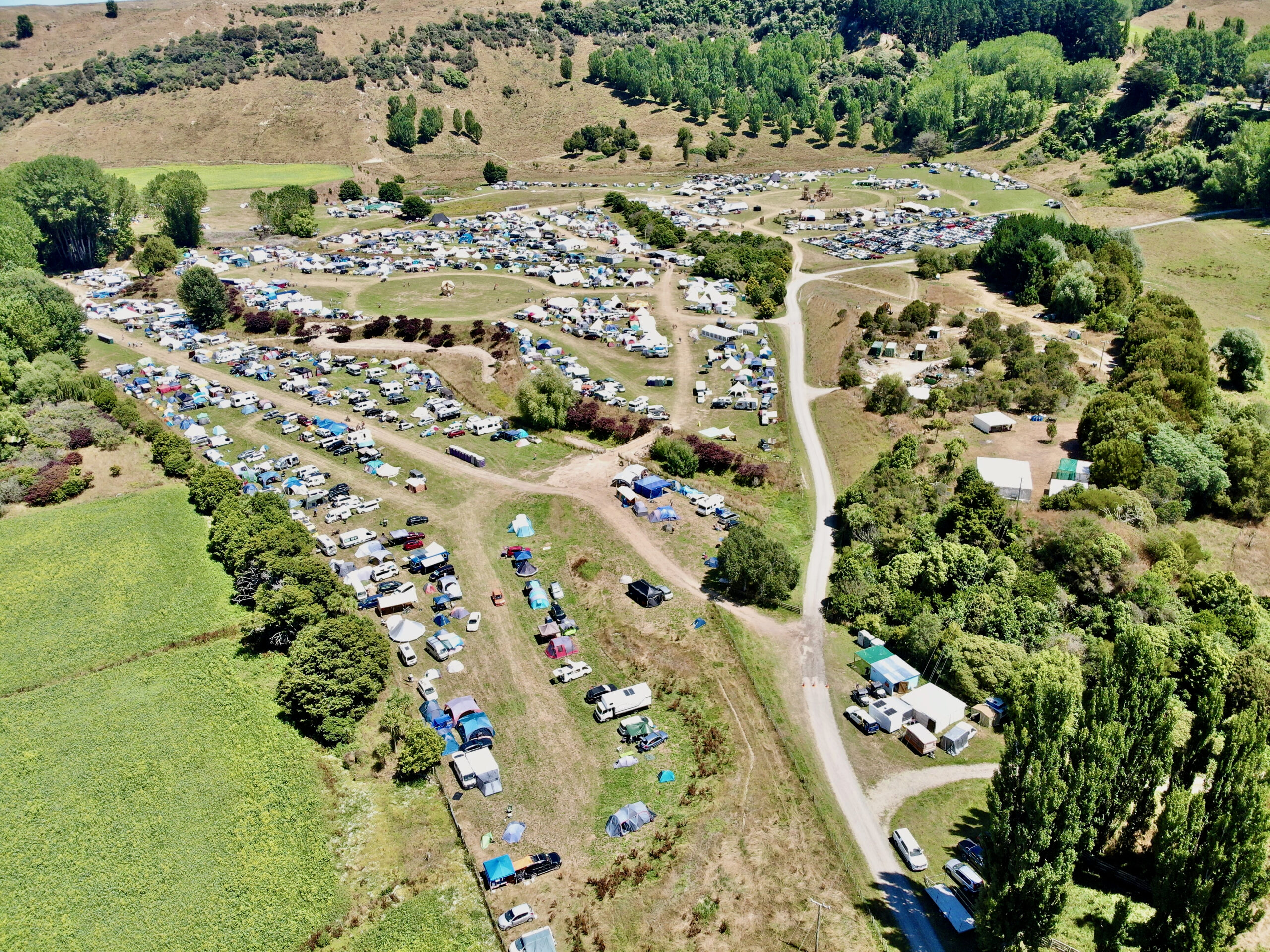 a drone shot of the KB site showing hundreds of tiny tents and campers, sprawling roads, a small effigy and temple, and lush green trees