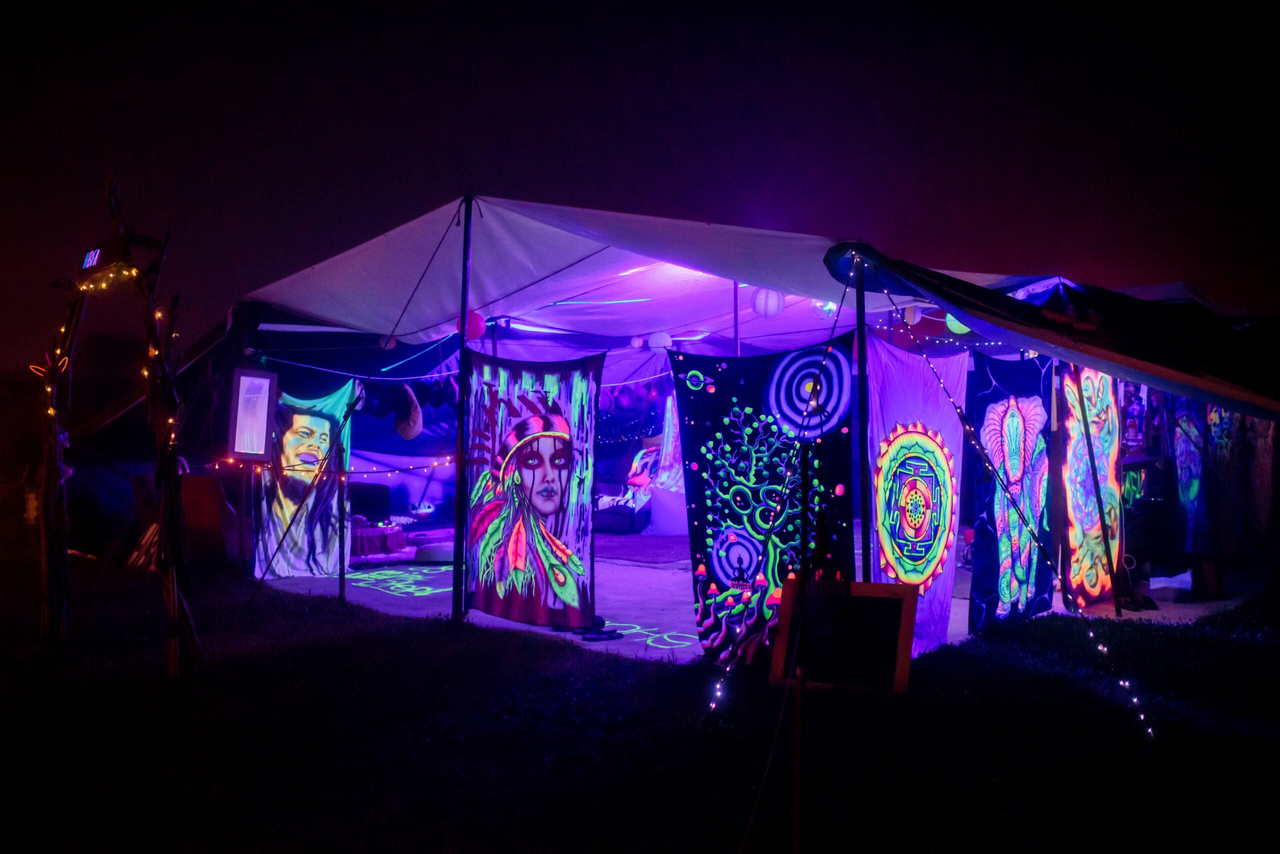 A glowing, blacklit array of funky art work hangs from a marquee in the dark