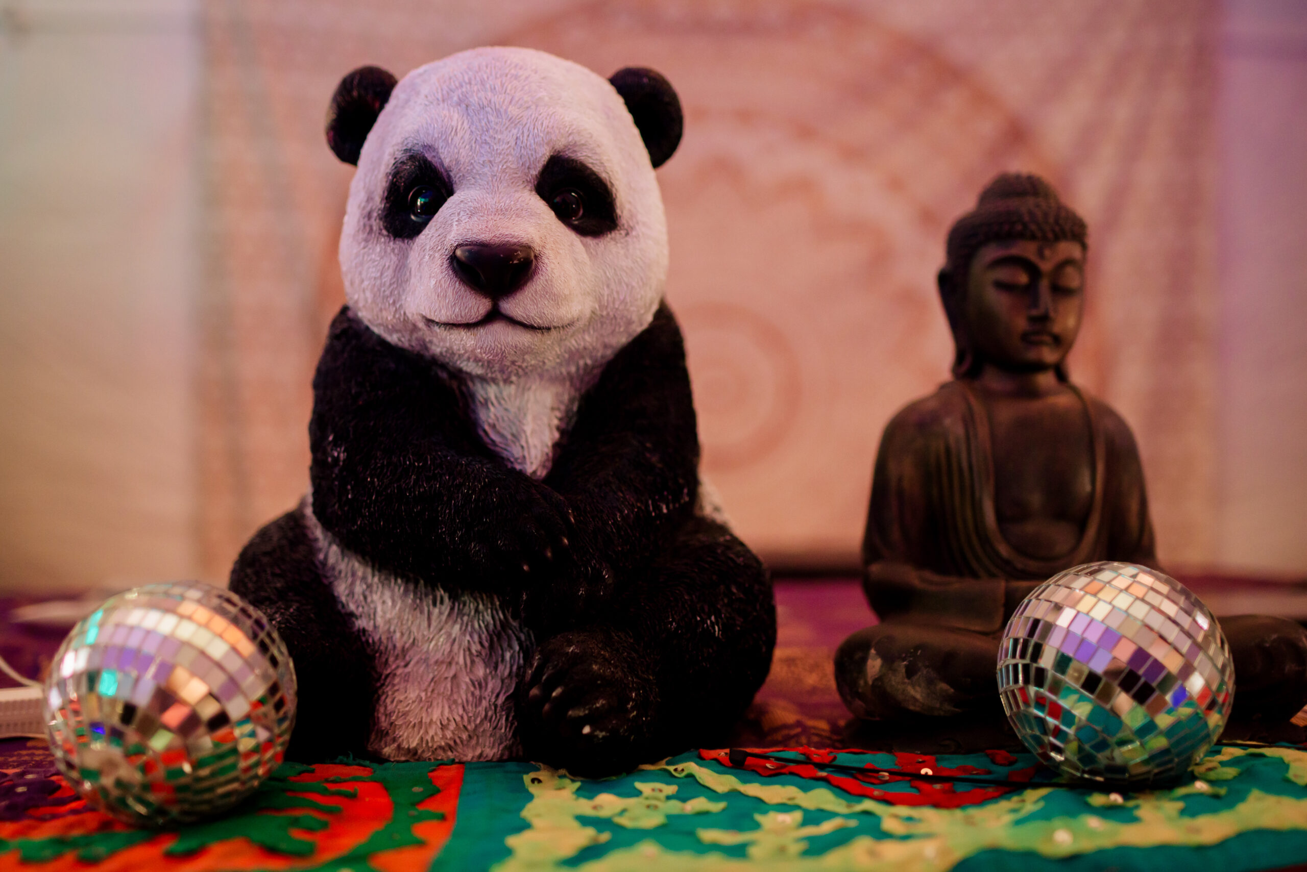 A stuffed panda and a Buddha sit next to each other in a tent with small shiny disco balls on either side of them