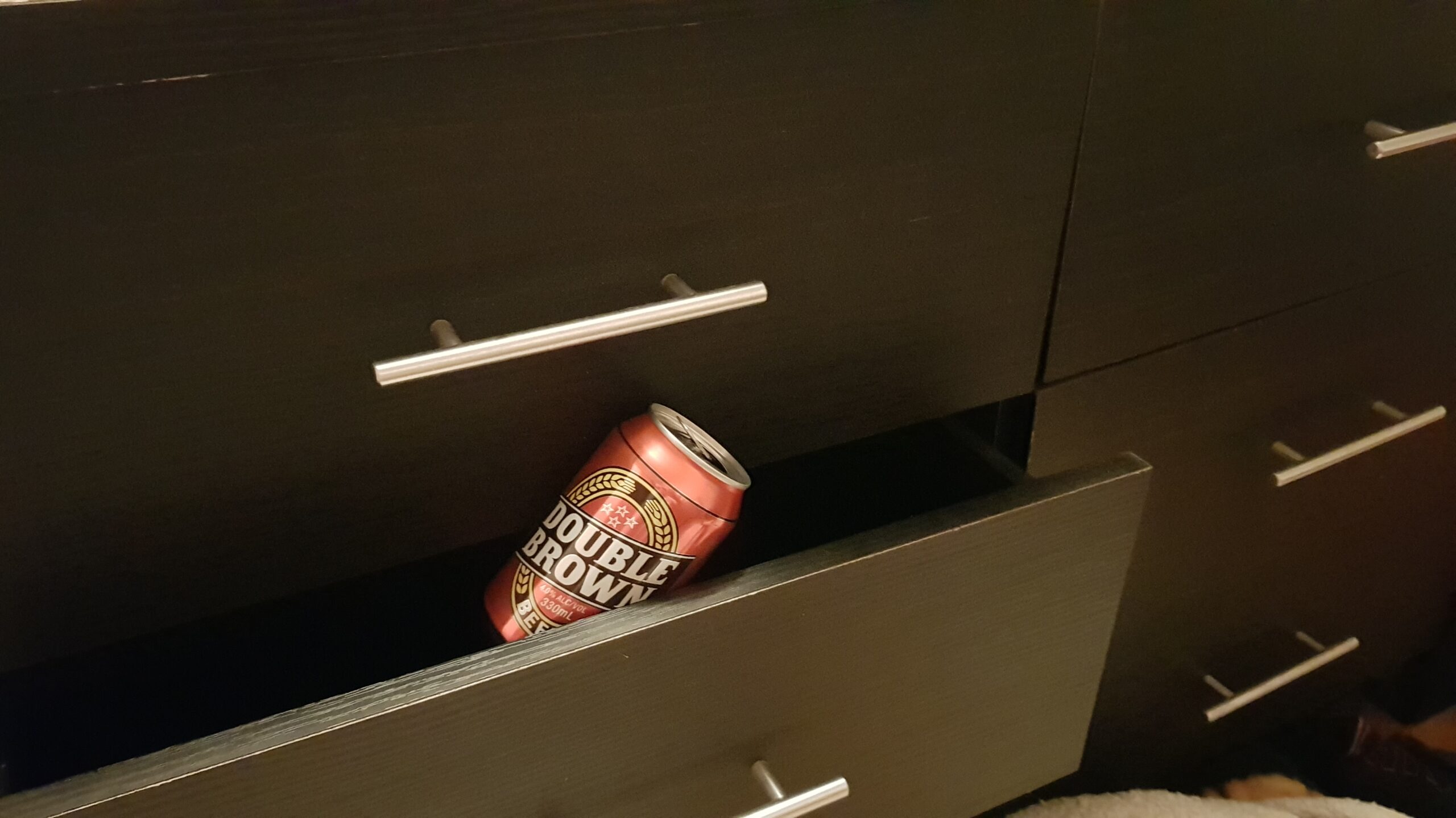 A can of Double Brown peeks out of a chest of dark coloured drawers