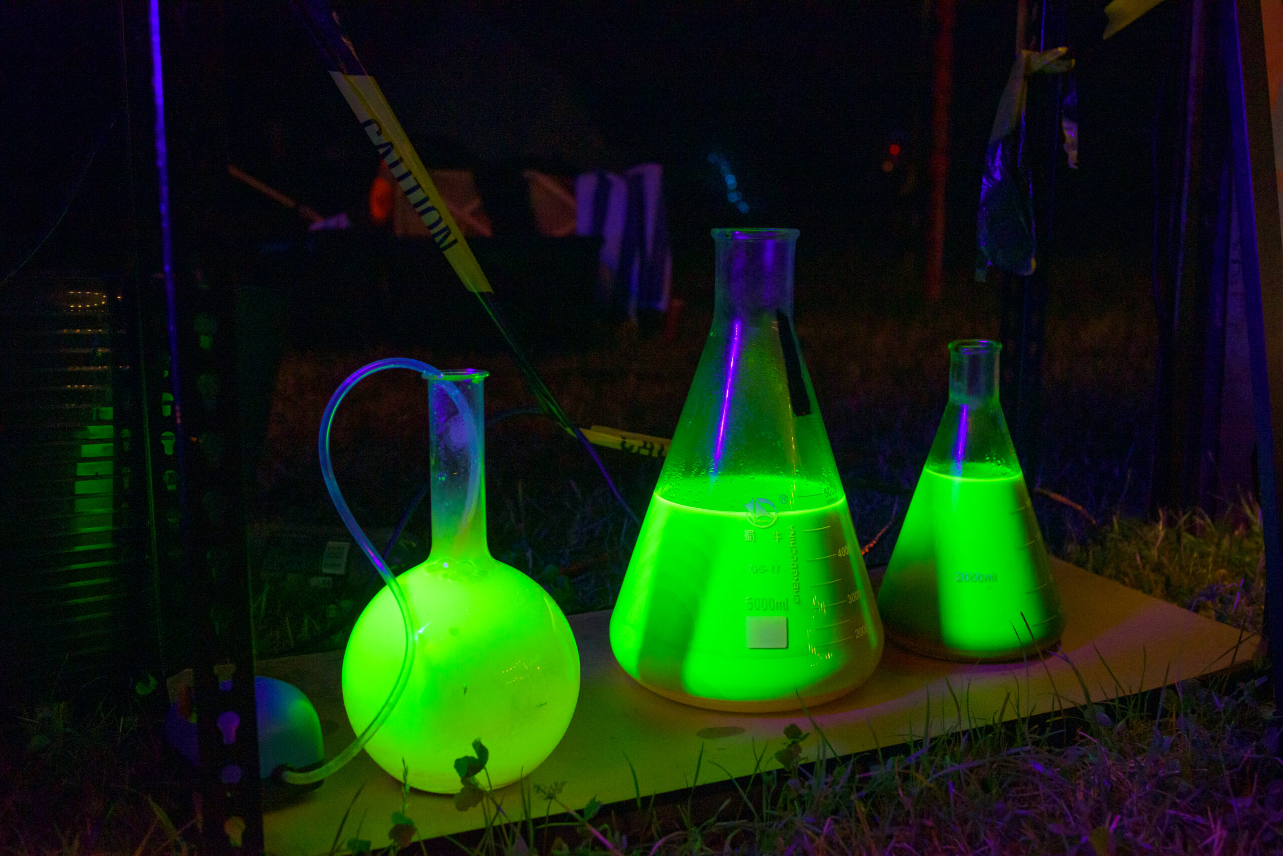 3 beakers full of glowing green/yellow liquid sit on a bar in a dark night