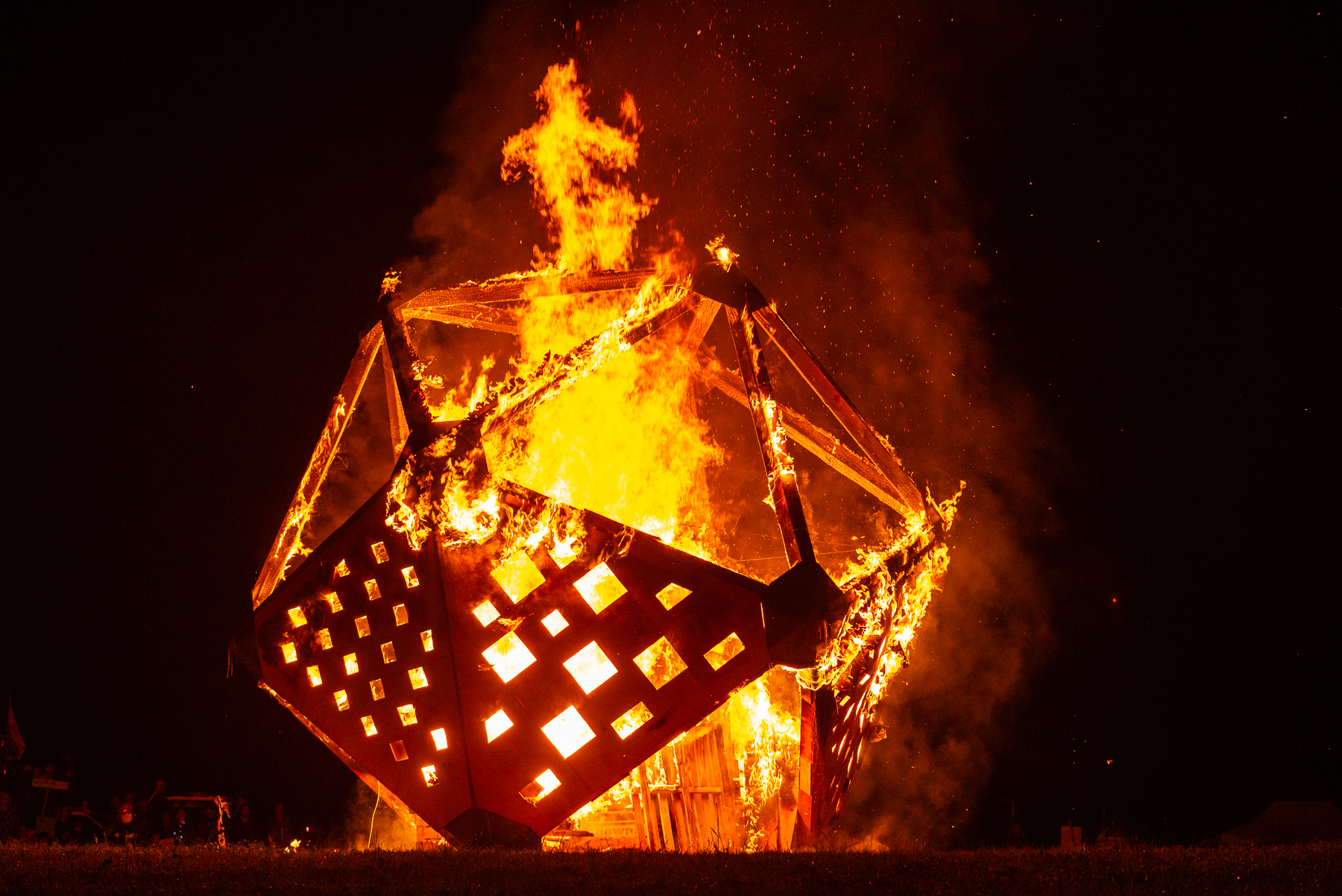 A giant wooden D20 Temple burns brightly against a black night