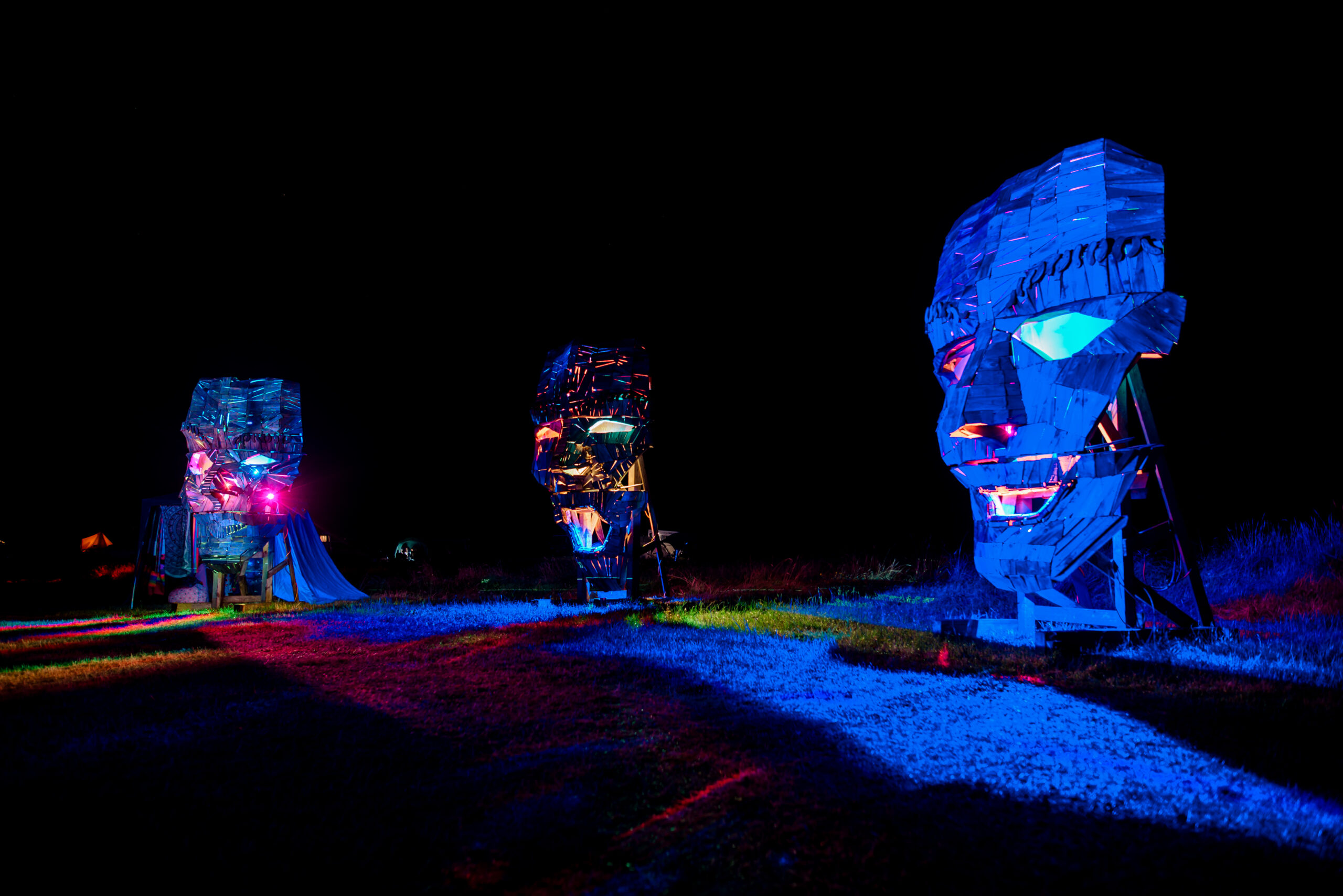 A glowing wooden art piece of three giant faces in the night