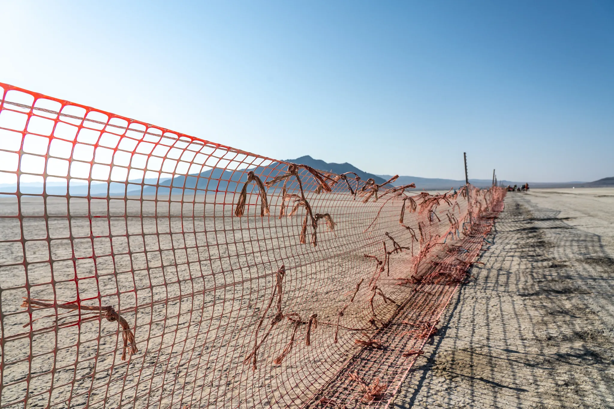 The bright orange trash fence sits on the dusty playa with blue sky in the background