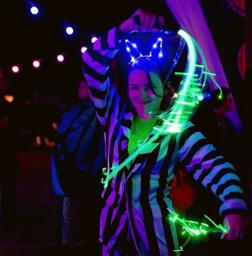 Alex dressed in a black and white striped onesie dancing with a glowing green pixel whip flow toy