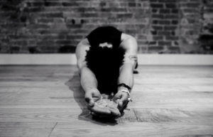 a person sits on the floor, head down, arms stretched in front of them with their hands cupped