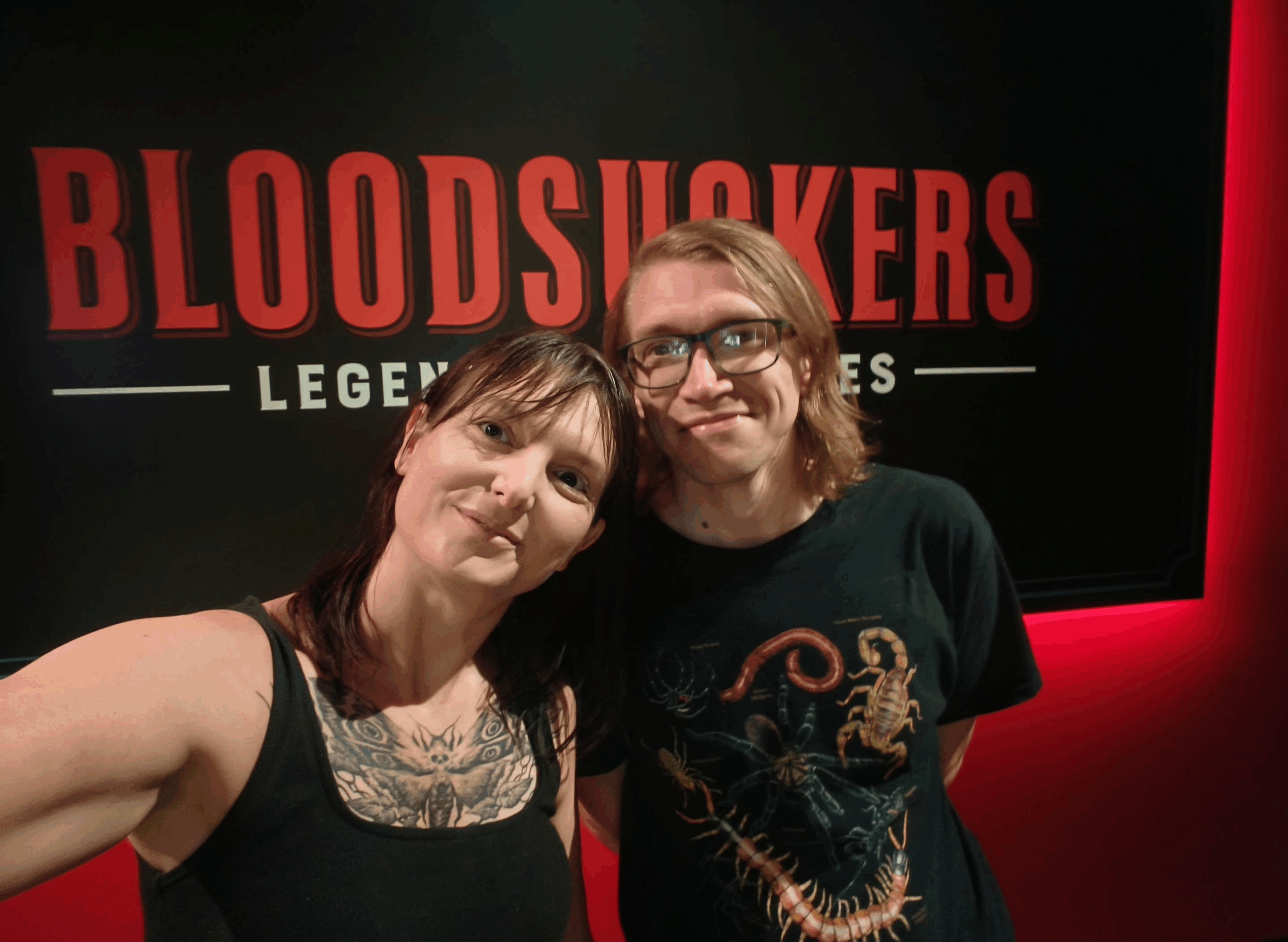 Temple builders Kym and David in front of a black sign with red lettering on a red wall