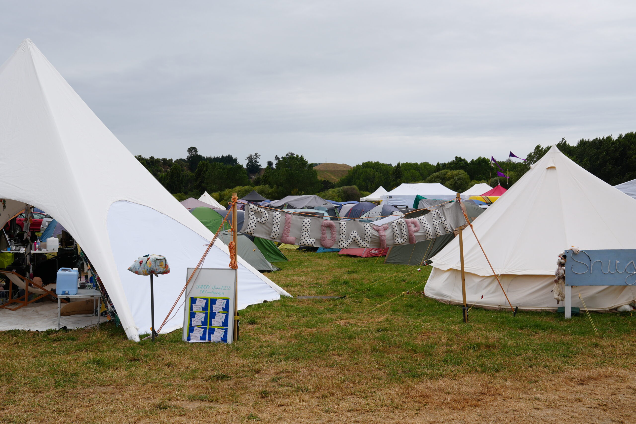 A white tent and white marquee sit on a paddock surrounded by other tents with a banner in between them reading 'Pillowtopia'
