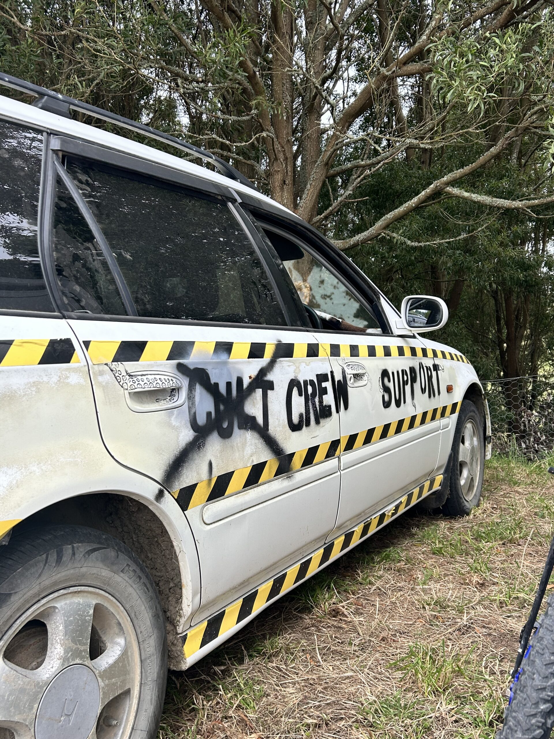 A white car with spray paint saying cult (crossed out) crew support.
